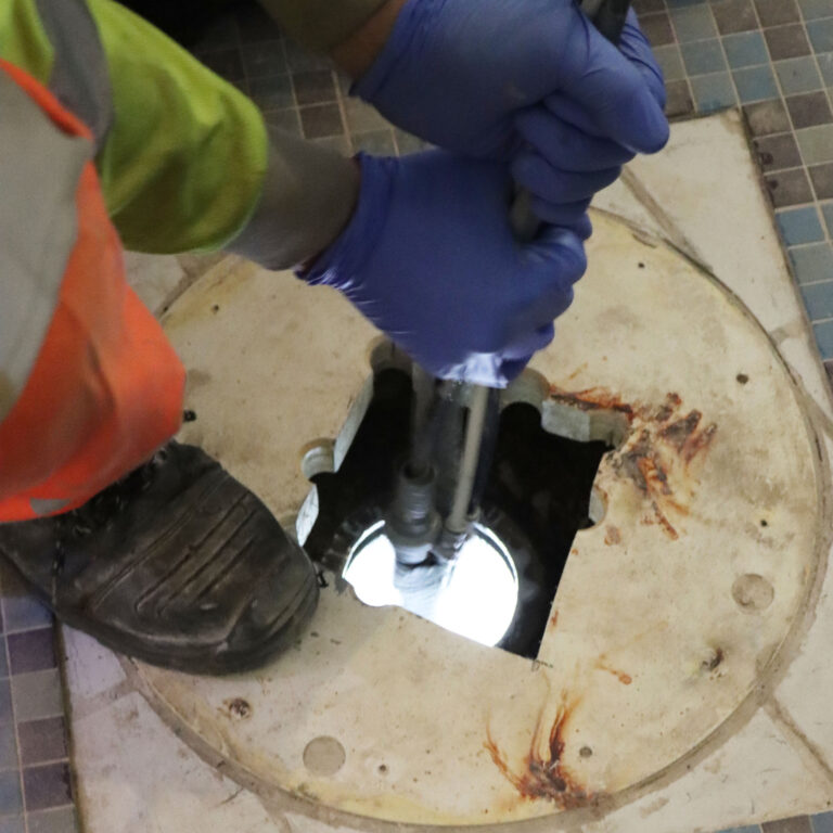 hands lowering inspection equipment into vertical pipe